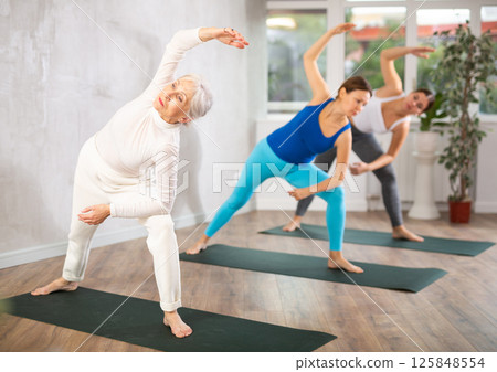 Focused older woman doing yoga poses with other women in yoga studio 125848554
