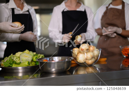 Group of cooking school students preparing fresh vegetables during a culinary class Group of cooking school students preparing fresh vegetables during a culinary class 125848639