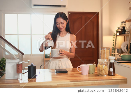 Charming Asian woman preparing her daily cup of coffee in a relaxed kitchen Charming Asian woman preparing her daily cup of coffee in a relaxed kitchen 125848642