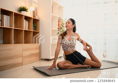 Young woman in activewear practicing yoga on mat in a bright living room 125848643
