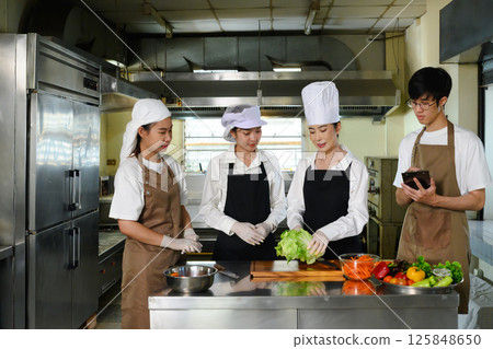 Cooking school instructor explaining food preparation techniques to students in a kitchen 125848650