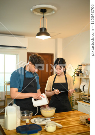 Man and woman cooking breakfast at home following digital recipe to make pancakes in a kitchen 125848706