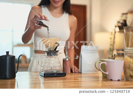 Close-up of hand pouring coffee grounds into a dripper on a wooden kitchen counter 125848719