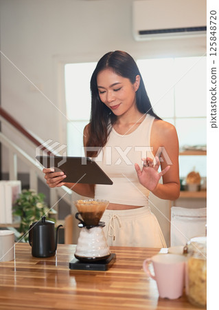 Happy asian woman using digital tablet while preparing pour over coffee at home 125848720