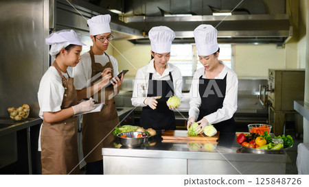 Chef guiding students in vegetable preparation during a hands-on culinary class 125848726
