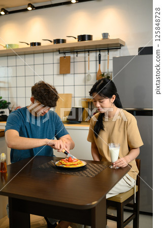 Young couple enjoying a homemade breakfast together with pancakes and a glass of milk Young couple enjoying a homemade breakfast together with pancakes and a glass of milk 125848728
