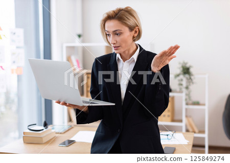Businesswoman wearing formal attire engaged in work with laptop indoors in modern office space Businesswoman wearing formal attire engaged in work with laptop indoors in modern office space 125849274
