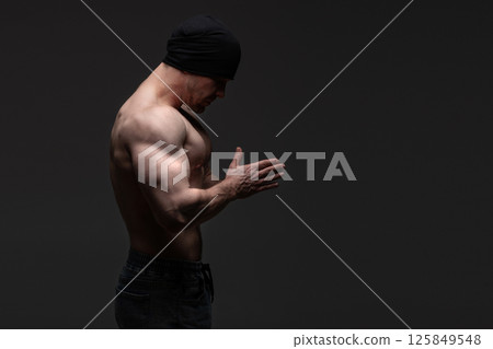 Shirtless man in black beanie with hands together, contemplative posture Shirtless man in black beanie with hands together, contemplative posture 125849548