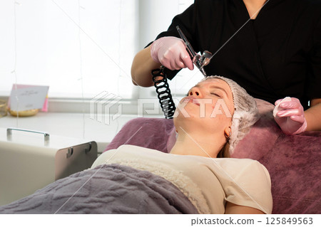 Esthetician administers facial microdermabrasion treatment on client's reclining spa bed 125849563
