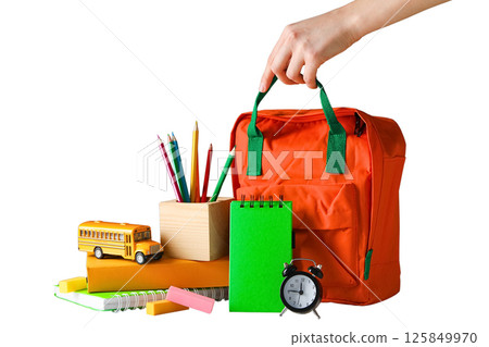 A hand reaches for an orange backpack among vibrant school supplies, isolated on white 125849970