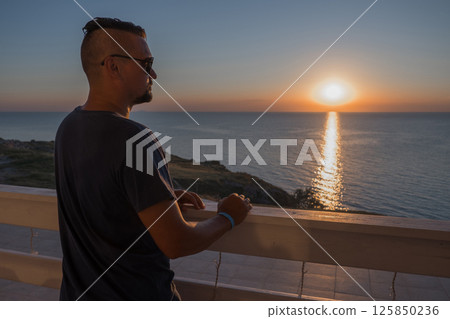 A man in sunglasses swims in a blue pool. Vacation at the hotel by the sea, sunset and mountains. Happy dad, family happiness. Muscles and a beautiful figure, black hair. High quality photo 125850236