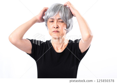 A senior woman with gray hair grimacing while holding her hand in her hair A senior woman with gray hair grimacing while holding her hand in her hair 125850378