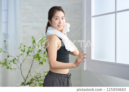 A woman in her twenties wearing yoga wear wiping sweat with a towel 125850683