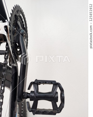 Close-up view of a black bicycle pedal attached to a crankset, showcasing intricate design and functionality 125851912