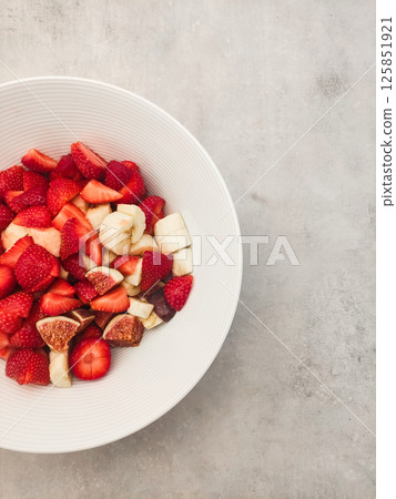 Freshly sliced strawberries, bananas, and figs in a white bowl on textured gray surface showcasing healthy snack concept Freshly sliced strawberries, bananas, and figs in a white bowl on textured gray surface showcasing healthy snack concept 125851921
