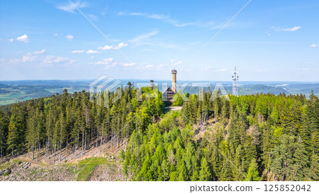 This aerial view highlights the picturesque Svatobor Lookout Tower set among lush forests in Czechia. The tower stands tall against a clear blue sky, offering breathtaking vistas. This aerial view highlights the picturesque Svatobor Lookout Tower set among lush forests in Czechia. The tower stands tall against a clear blue sky, offering breathtaking vistas. 125852042