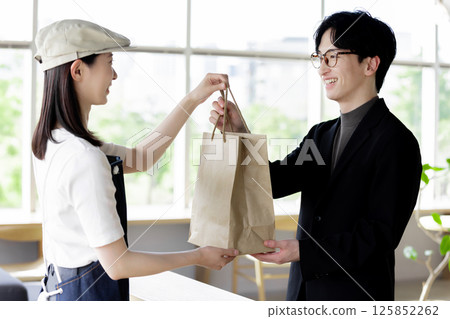 A female clerk at a cafe handing an order to a customer at the counter 125852262