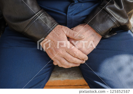 The man's aged hands, firmly folded. The man's trembling fingers.  125852587