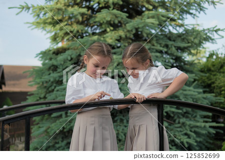 The girls watch the snail, holding their breath. Matching skirts flutter lightly, adding a sense of movement.  125852699