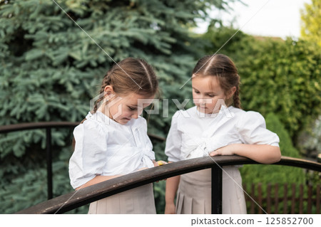 The girls stand very close, leaning toward the tiny snail. The harmony in their outfits and hairstyles highlights their kinship 125852700