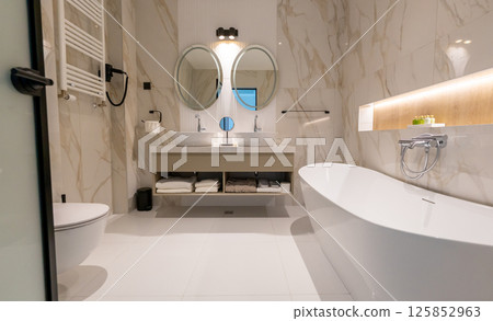 A modern hotel bathroom with freestanding bathtub, double sink, toilet and round mirrors in elegant interior A modern hotel bathroom with freestanding bathtub, double sink, toilet and round mirrors in elegant interior 125852963