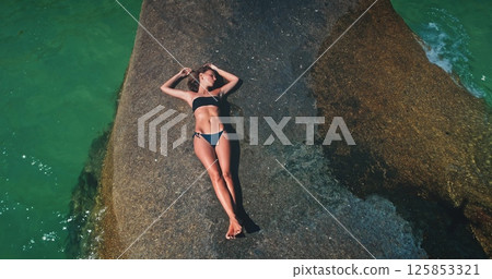 A person enjoys the warmth of the sun while lounging on a rock beside clear turquoise waters. The serene atmosphere creates a peaceful escape, perfect for unwinding. A person enjoys the warmth of the sun while lounging on a rock beside clear turquoise waters. The serene atmosphere creates a peaceful escape, perfect for unwinding. 125853321