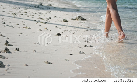 Woman walks barefoot on a sunny beach, leaving footprints in the sand as waves kiss the shore, embodying freedom and relaxation in a tropical paradise Woman walks barefoot on a sunny beach, leaving footprints in the sand as waves kiss the shore, embodying freedom and relaxation in a tropical paradise 125853325