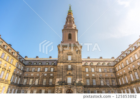 Christiansborg Palace, located on Slotsholmen, showcases stunning architecture under a clear blue sky. Visitors admire its historic significance and grandeur during their exploration. 125853892