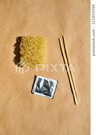 Dry instant noodles with wooden chopsticks and seasoning packet over brown background. Dry instant noodles with wooden chopsticks and seasoning packet over brown background. 125854394