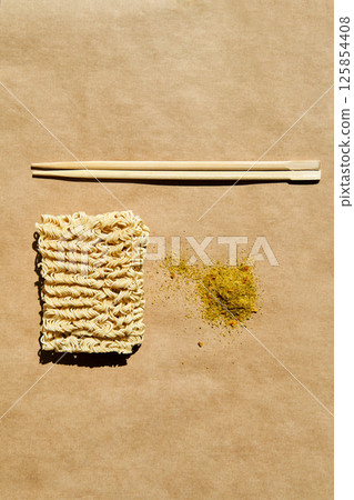 Dry instant noodles with wooden chopsticks and seasoning over brown background. Dry instant noodles with wooden chopsticks and seasoning over brown background. 125854408