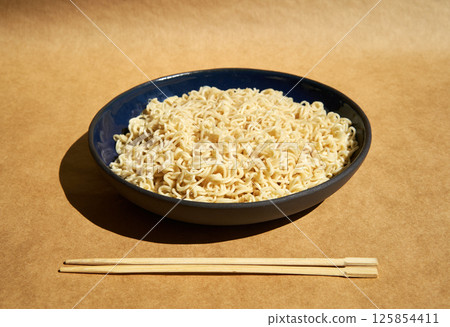 Bowl of cooked instant noodles with wooden chopsticks over brown background. 125854411