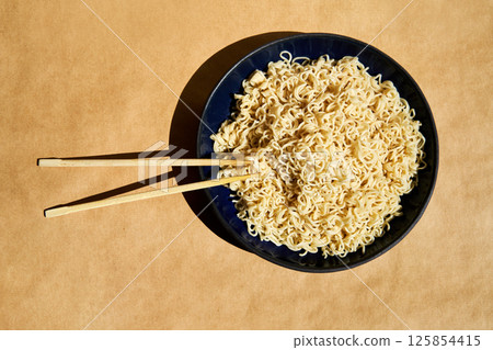 Bowl of cooked instant noodles with wooden chopsticks over brown background. 125854415