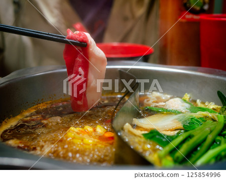 human hand using chopsticks hold meat over Sichuan mala hotpot shabu on restaurant table. human hand using chopsticks hold meat over Sichuan mala hotpot shabu on restaurant table. 125854996