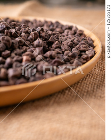 Raw Dark Brown Chickpeas (Kala Chana) on a rustic wooden table. Dry Balck chickpea (ceci neri) background close up. Raw Dark Brown Chickpeas (Kala Chana) on a rustic wooden table. Dry Balck chickpea (ceci neri) background close up. 125855173