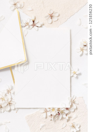 Blank card and envelope near white cherry flowers top view, spring wedding mockup 125856230