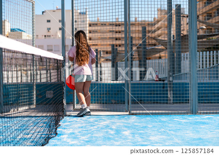 Child with paddle on sunny sport court, urban landscape behind. Child with paddle on sunny sport court, urban landscape behind. 125857184