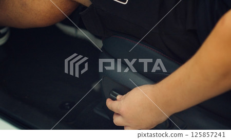 Close up of man in car adjusting driver seat using buttons. Person in vehicle chair that can be raised, lowered, tilted, moved forwards and backwards to suit the comfort of driver Close up of man in car adjusting driver seat using buttons. Person in vehicle chair that can be raised, lowered, tilted, moved forwards and backwards to suit the comfort of driver 125857241