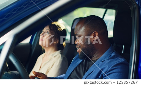 Clients going on test drive before buying car, receiving keys from salesman after being happy with pedals and seat adjustments. Customers evaluate how vehicle feels before buying from agent, camera A 125857267