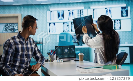 Indian medical staff and male patient engaging in a check up exam with diagnostic tools and test results for scan interpretation. Showcasing healthcare practices and research. Camera B. Indian medical staff and male patient engaging in a check up exam with diagnostic tools and test results for scan interpretation. Showcasing healthcare practices and research. Camera B. 125857279