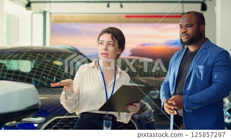 Saleswoman in dealership negotiating price and extra car features to help solidify deal, earning commission bonuses on every sale. Agent persuading hesitant customer to buy vehicle, camera A 125857297