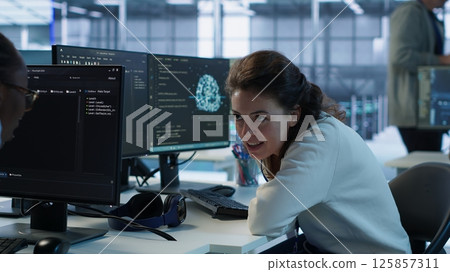 Happy technician chatting with colleague while doing maintenance on artificial intelligence neural networks. Jolly admin talking with coworker while using AI systems aiding processing, camera A Happy technician chatting with colleague while doing maintenance on artificial intelligence neural networks. Jolly admin talking with coworker while using AI systems aiding processing, camera A 125857311