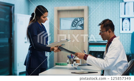 Physician expert reviewing x ray scan results in his medical office, providing diagnostic for a sick patient. Medic studying hospital records and sharing his expertise, healthcare industry. Camera A. Physician expert reviewing x ray scan results in his medical office, providing diagnostic for a sick patient. Medic studying hospital records and sharing his expertise, healthcare industry. Camera A. 125857349