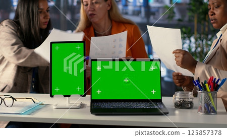 Team of female shareholders meeting to discuss expansion plan next to isolated mockup, sharing their ideas to use more funds on a development project. Working for success and productivity. Camera A. Team of female shareholders meeting to discuss expansion plan next to isolated mockup, sharing their ideas to use more funds on a development project. Working for success and productivity. Camera A. 125857378