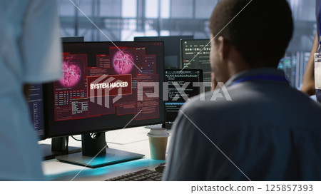 Engineers seeing system hacked popup on PC screen in data center, requesting help from cybersecurity team. Server farm worker seeing security incidents affecting network system, camera A 125857393