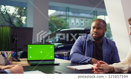 Salesman using isolated screen laptop to present car addons options to clients, trying to sway them to make purchase. Showroom agent offers warranty to customers, holding chroma key notebook, camera B 125857394