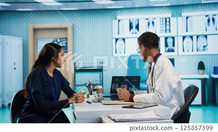 Indian general practitioner and patient engage in a medical consultation with diagnostic tools and x ray text results for scan interpretation. Showcasing healthcare practices and research. Camera B. 125857399