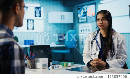 Medical expert and patient discussing diagnostic results in a modern cabinet, establishing advanced healthcare tools to present x ray imaging scans. Insurance management. Camera B. Medical expert and patient discussing diagnostic results in a modern cabinet, establishing advanced healthcare tools to present x ray imaging scans. Insurance management. Camera B. 125857406