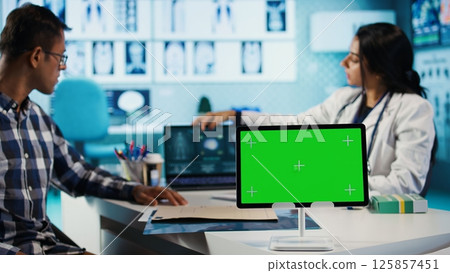 Female general practitioner and patient looking at green screen on tablet, recommending pills and drugs during check up. Indian people discussing about diagnostic report and remedy. Camera B. Female general practitioner and patient looking at green screen on tablet, recommending pills and drugs during check up. Indian people discussing about diagnostic report and remedy. Camera B. 125857451