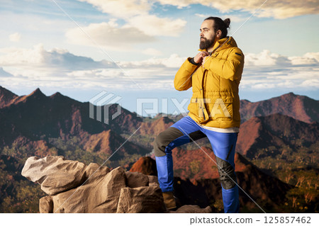 Male explorer embraces the solitude of high altitude wilderness, climbing on top of the mountain for fresh air and a scenic background. Mindfulness and relaxation in the nature. 125857462