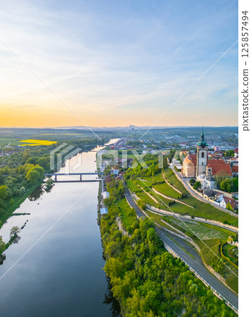 An aerial view captures Melnik City and its chateau perched above the Labe River in Czechia during sunset. The landscape showcases lush greenery and the serene river. An aerial view captures Melnik City and its chateau perched above the Labe River in Czechia during sunset. The landscape showcases lush greenery and the serene river. 125857494